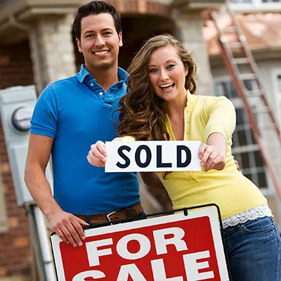 Image of couple in front of real estate sign holding a SOLD sign
